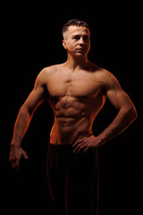 Fototapeta premium Adult male athlete bodybuilder posing on a orange light