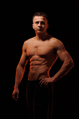 Fototapeta premium Adult male athlete bodybuilder posing on a orange light