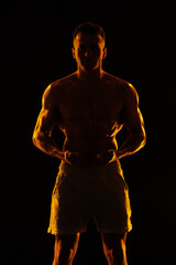 Fototapeta premium Adult male athlete bodybuilder posing on a orange light 