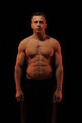 Adult male athlete bodybuilder posing on a orange and blue light