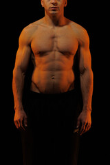 Adult male athlete bodybuilder posing on a orange and blue light