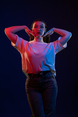 Young girl posing and moving in a black studio with colored light
