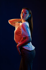 Young girl posing and moving in a black studio with colored light