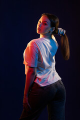 Young girl posing and moving in a black studio with colored light