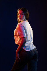 Young girl posing and moving in a black studio with colored light