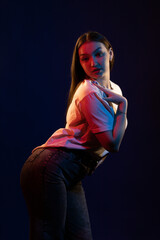Young girl posing and moving in a black studio with colored light	