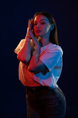 Young girl posing and moving in a black studio with colored light	