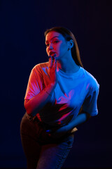 Young girl posing and moving in a black studio with colored light	