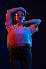 Young girl posing and moving in a black studio with colored light	