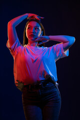 Young girl posing and moving in a black studio with colored light	