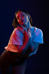 Young girl posing and moving in a black studio with colored light	
