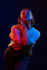 Young girl posing and moving in a black studio with colored light	