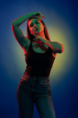 Young girl posing and moving in a black studio with colored light	