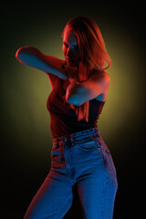 Young girl posing and moving in a black studio with colored light	