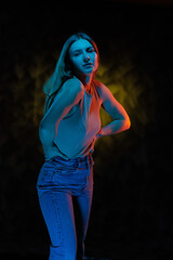 Young girl posing and moving in a black studio with colored light