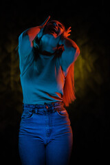 Young girl posing and moving in a black studio with colored light