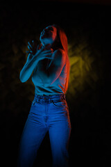 Young girl posing and moving in a black studio with colored light	
