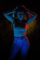 Young girl posing and moving in a black studio with colored light	