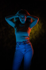 Young girl posing and moving in a black studio with colored light	