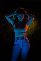 Young girl posing and moving in a black studio with colored light	