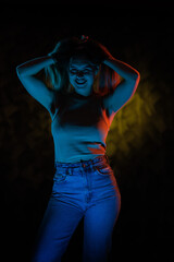 Young girl posing and moving in a black studio with colored light	