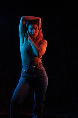 Young girl posing and moving in a black studio with colored light	