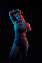 Young girl posing and moving in a black studio with colored light	