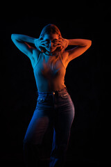 Young girl posing and moving in a black studio with colored light	