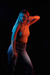 Young girl posing and moving in a black studio with colored light	