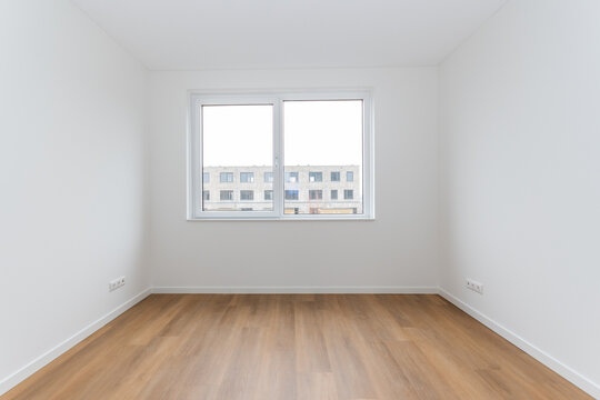interior empty basic bedroom in modern new build residential smart house. Glass window is neighboring building over the road. Plain white walls and wood effect vinyl flooring make blank canvas