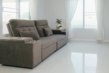 Bright living room interior featuring a sleek gray couch with pillows and drink holders. The white floors and sheer curtains create a clean and inviting space, perfect for relaxation.