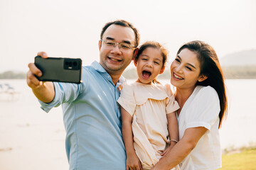 Asian family taking selfie picture with smartphone outdoor nature park, Happy smile father mother and child daughter taking photo with mobile phone together, Tourist lifestyle people leisure activity