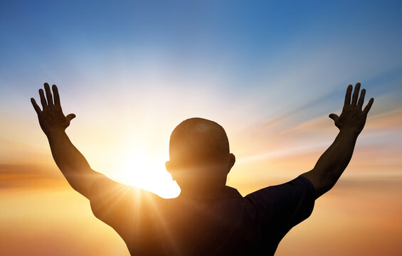 Silhouette of a man raising his hands up against sunset sky 