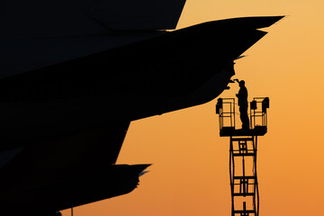 Aircraft mechanic repairing aircraft at sunset