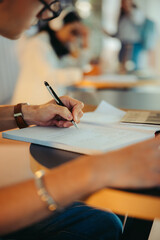 Close-up of a person writing homework assignment in a notebook at a desk with focus on hand and pen