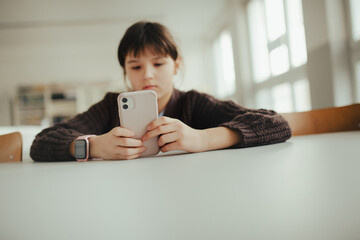 Young schoolgirl sitting in a science lab with a phone in her hand, waiting for classmates.