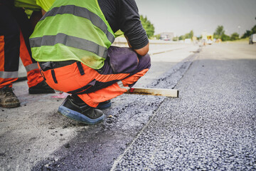 Construction worker measuring fresh asphalt to ensure it’s level, ensuring precision and quality...