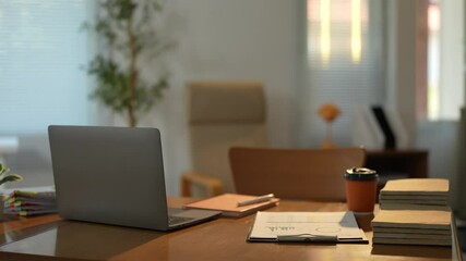 Sunlight illuminates a modern office desk featuring a closed laptop, stacked documents, a takeaway coffee cup, and a clipboard with charts, creating a serene workspace ambiance