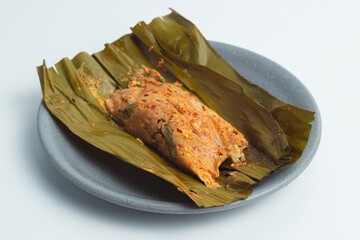 Pepes Tahu Jamur, seasoned tofu and mushroom, wrapped in banana leaves then steamed and then grill a while. Serving on wooden table or motif plate.