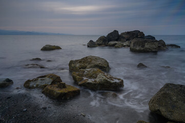 Calm waves gently lap against rugged stones on a serene shoreline at dusk near tranquil waters