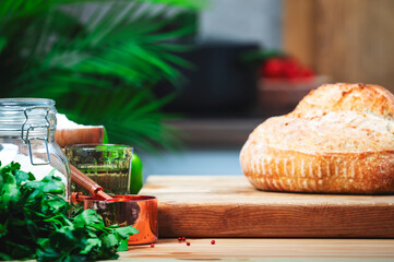 Rustic whole grain wheat sourdough bread on wooden cutting board.. Kitchen table with vegetables and herbs against the background of modern classic kitchen