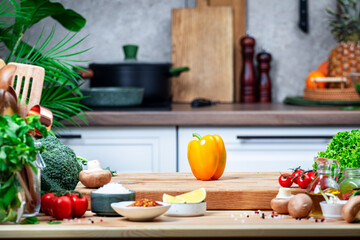 Healthy eating, cooking, food blogging background. Orange paprika on oak cutting board with vegetables, herbs and spices on cozy kitchen with wooden table, kitchenware and ingredients for cooking