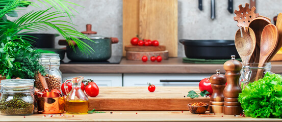 Chef cuts cherry tomato. Cozy kitchen with wooden table, kitchenware, vegetables, herbs and ingredients for cooking. Healthy vegan food, culinary, recipes, food blogging
