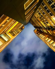 Night view from bottom to top of multi-story buildings illuminated with yellow light against the sky.
