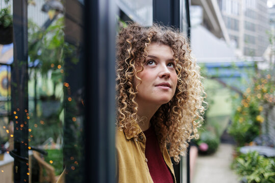 Thoughtful botanist looking from window at plant nursery - Powered by Adobe