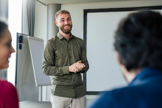 Smiling young businessman giving presentation to colleagues at office