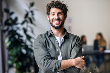 Smiling businessman standing with arms crossed in office