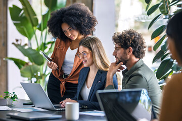 Blond businesswoman using laptop and talking with colleagues in office