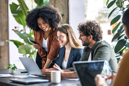 Smiling multiracial business colleagues discussing over laptop in office