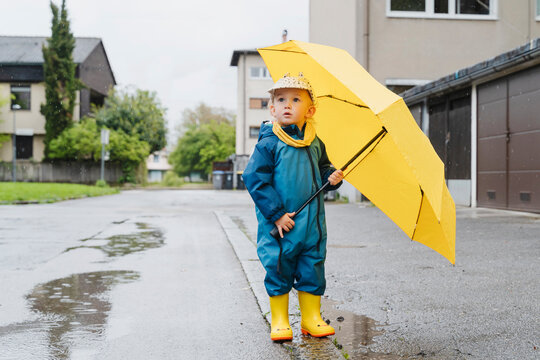 Child with yellow umbrella standing outdoors on a rainy day